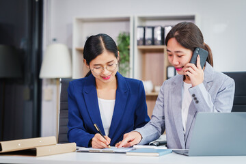 Fototapeta premium Two Asian businesswomen collaborate on stock market strategies and financial services, exchanging comments and suggestions on loan applications and investment opportunities.