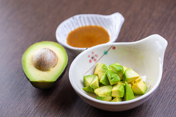 A photo of a bowl of avocado chunks and a bowl of soy sauce on a wooden table.