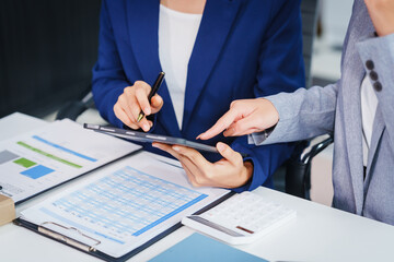 Two Asian businesswomen collaborate on stock market strategies and financial services, exchanging...
