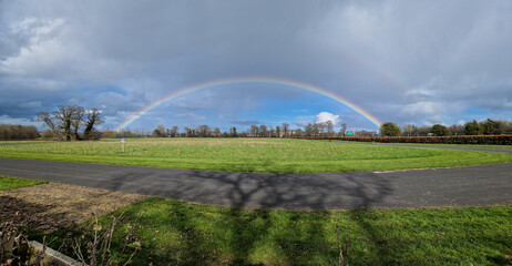 Capturing the magic of nature, a vibrant rainbow arches gracefully over the serene Corkagh Park,...