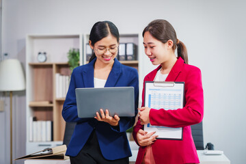 Two Asian businesswomen collaborate on stock market strategies and financial services, exchanging...