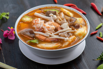 A bowl of Tom Yum soup with shrimp, mushrooms, and vegetables.