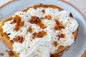 A close-up image of a piece of toast with whipped cream and brown sugar crystals on top.