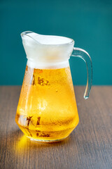 A pitcher of beer on a wooden table with a dark green background.