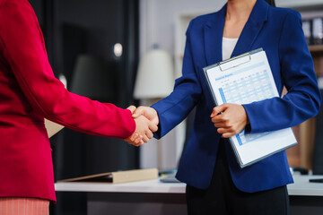 Two Asian businesswomen shake hands, collaborating on financial matters, discussing comments and suggestions regarding the stock market, loans, securities law, and investment strategies.