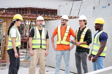 Engineer wearing safety helmet stands in meeting to plan work at construction site.