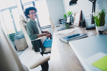 Photo of cheerful handsome agent dressed khaki shirt eyewear send emails modern gadget indoors...