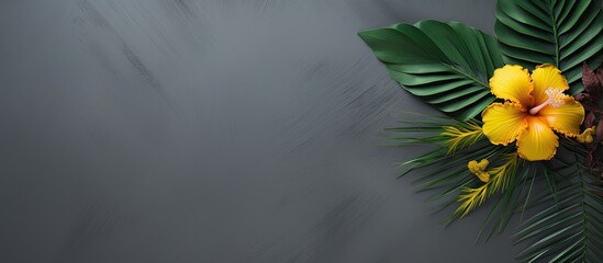On a green palm leaf a yellow flower and a flower petal pattern on a gray background with a copy of the space Layout for your ideas Flat lay - Powered by Adobe