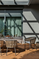 Simple composition of terrace interior with table, chairs, brown tablecloth, tableware, big window,...