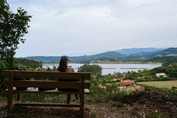 Woman records with her mobile phone sitting on a bench a landscape with mountains and villages. Concept of hiking, capturing moments.