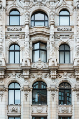 Obraz premium Ornate architectural facade with intricate carvings and arched windows reflecting the city, showcasing historic European-style design.