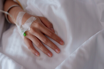 Adult hand resting on hospital bed, intravenous line attached, highlighting sterile environment and...