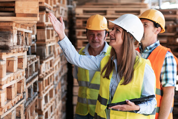 Wooden industry workers walk with their supervisor on the factory yard, checking numbers and quality of products. They discuss production details and ensure standards are met.
