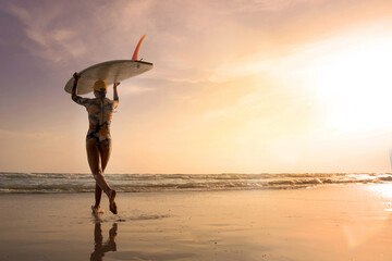 Female surfer wearing a swimsuit holding a surfboard on her head, Running towards the waves is fun...