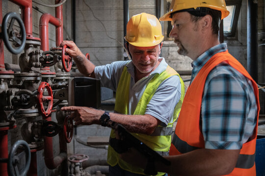 Two maintenance workers are adjusting the pressure in the pipes to ensure the factory operates normally. They carefully monitor the instruments and make necessary adjustments.