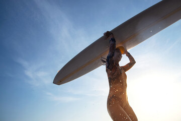 Female surfer wearing a swimsuit holding a surfboard on her head, running towards the waves is fun...