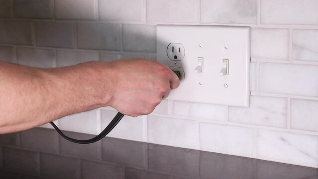 inserting a plug into a wall socket outlet and plugging in a power cord