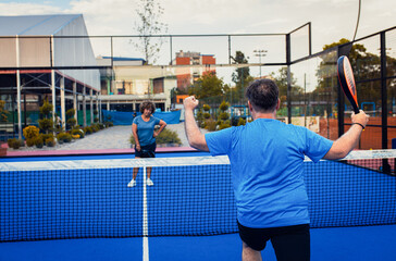 Rear view of male adult padel player celebrates victory in game on outdoor court.