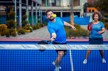 Mixed adult couple palying padel on outdoor court.