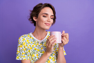 Photo of pretty young woman smell coffee empty space wear t-shirt isolated on violet color...