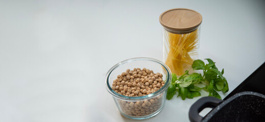 Raw chickpeas in a glass bowl on a white table with basil