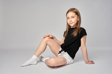 Full length portrait of a cute girl, wearing white shorts and black shirt, sitting on white background