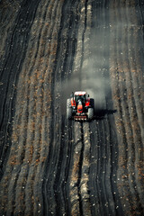 Aerial view of a tractor plowing dark soil in neat lines.