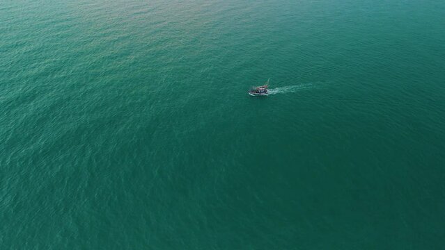 Aerial view lonely small fishing boat trawler sails along the sea surface at evening for night seafood fishing.