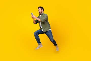 Full size photo of nice young man jump run phone wear shirt isolated on yellow color background