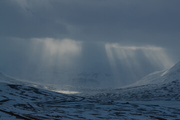 Sunlight streaming through clouds over snowy mountains