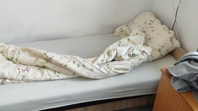 Unmade bed and room in a student dormitory or inexpensive hostel.