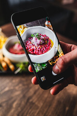 Close-up of a hand holding a smartphone, capturing a colorful dish with garnish. Blurred food items...