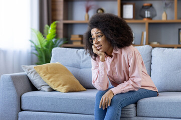 A worried woman sitting on a couch, feeling stressed and anxious in a cozy living room setting.