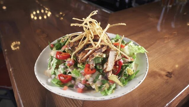 Closeup of spinning white plate with fresh Caesar salad on a wooden restaurant table