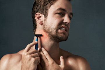 Razor, shaving or man in studio with pain or hair removal for skincare tools, face grooming or cosmetics. Uncomfortable, rough irritation and model on grey background for neck shaver and wellness