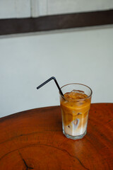 iced oatmilk coffee latte in a transparent glass, served on wooden table with white wall background
