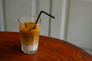 iced oatmilk coffee latte in a transparent glass, served on wooden table with white wall background