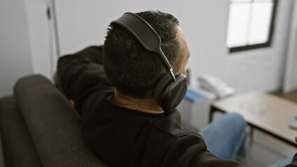 A relaxed man listening to music with headphones while sitting on a couch in a modern living room.