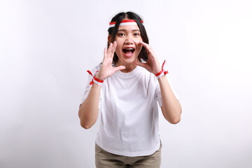 Young Asian woman wearing red white flag ribbon shouting loud at the camera, telling about good sale offer isolated over white background. Celebrate Indonesian independence day on 17 August