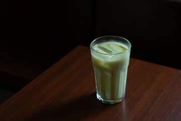 iced avocado frappe in transparent glass, served on wooden table, with dark moody background