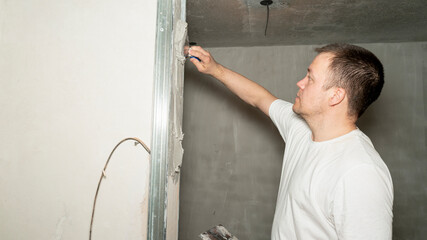 Worker is putting a gypsum plaster on a wall using a spatula. 