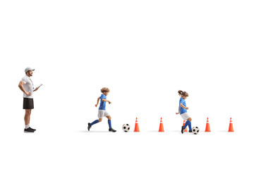 Fototapeta premium Coach watching a boy and girl leading a football between obstacle cones