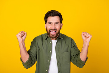 Photo of nice young man raise fists wear khaki shirt isolated on yellow color background