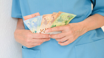 Close-up of the hands of a nurse in a turquoise uniform holding and counting money. Concept of...
