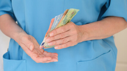 Close-up of the hands of a nurse in a turquoise uniform holding and counting money. Concept of...