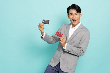 Young Asian businessman in grey suit showing two credit card isolated on green background