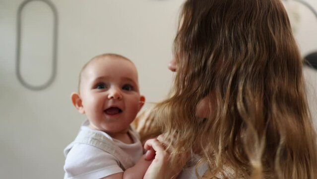 A young mom holds her little child and dances with her. The mother and child dance, laughing and smiling.