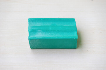 A green dishwash soap bar on a light wooden surface. Top view.