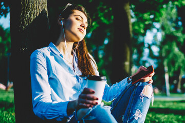 Young woman in casual wear relaxing with favorite music in earphones sitting with closed eyes in...