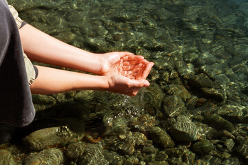 A woman touches the water with her hands. Women's hands collect water in their hands near the...